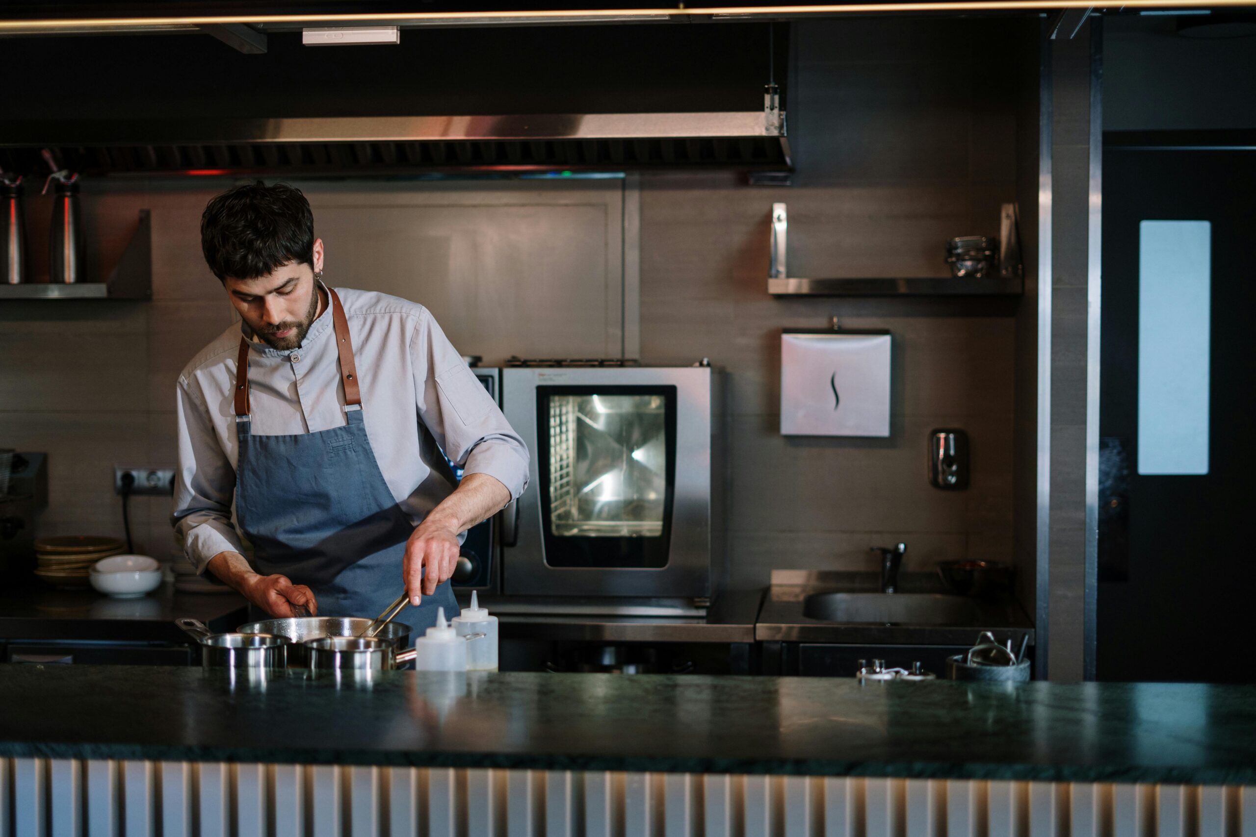 A chef in a blue apron cooking at a modern open kitchen counter.