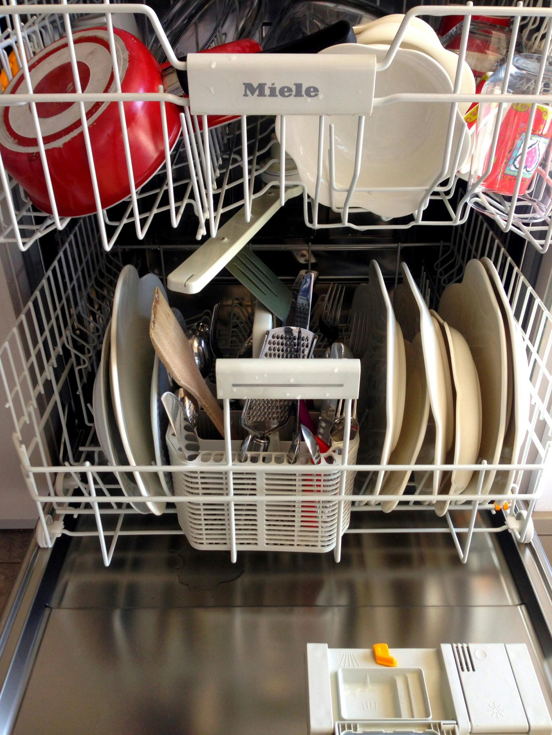 Open dishwasher filled with clean dishes and kitchenware, ready for unloading.